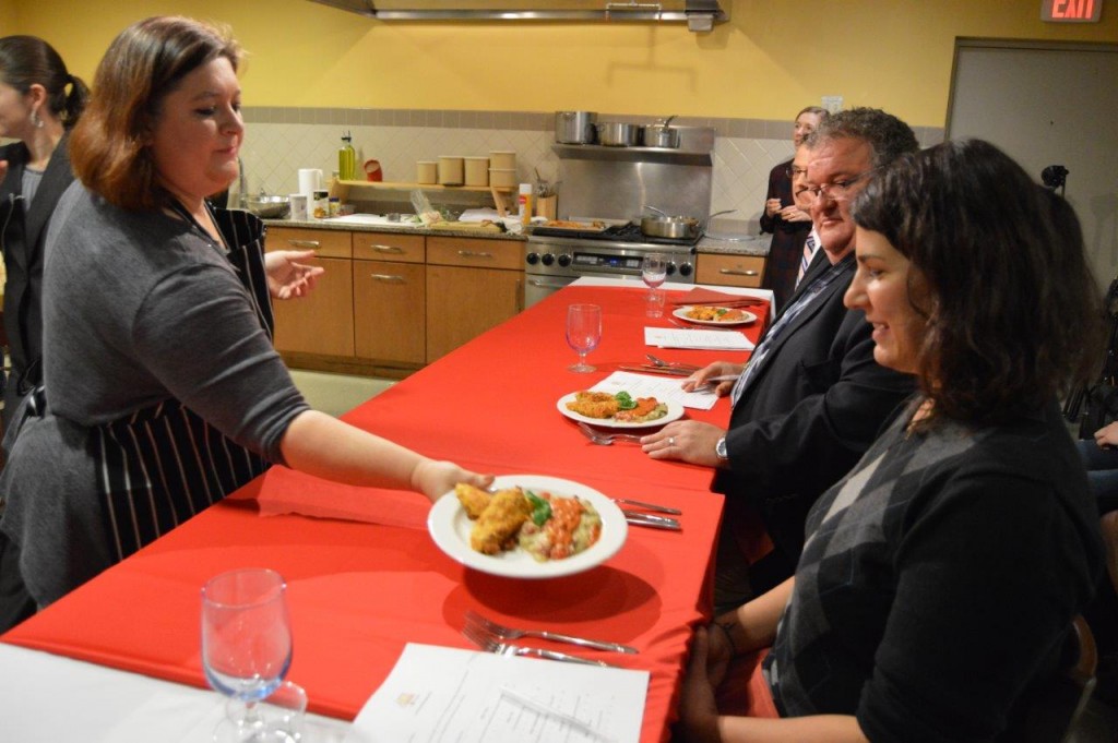 Jeanette Souther (left) presents her winning dish to the judging panel. Front right: Seven Days Food Writer Suzanne Podhaizer. Center right: WOKO On-Air Personality Rod Hill. Back right: ABC 22/FOX44 Anchor Bernie Lange. 